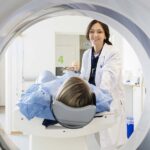 A smiling doctor positioning a patient on a CT scanner table, a procedure often compared to an MRI in terms of how long it takes.