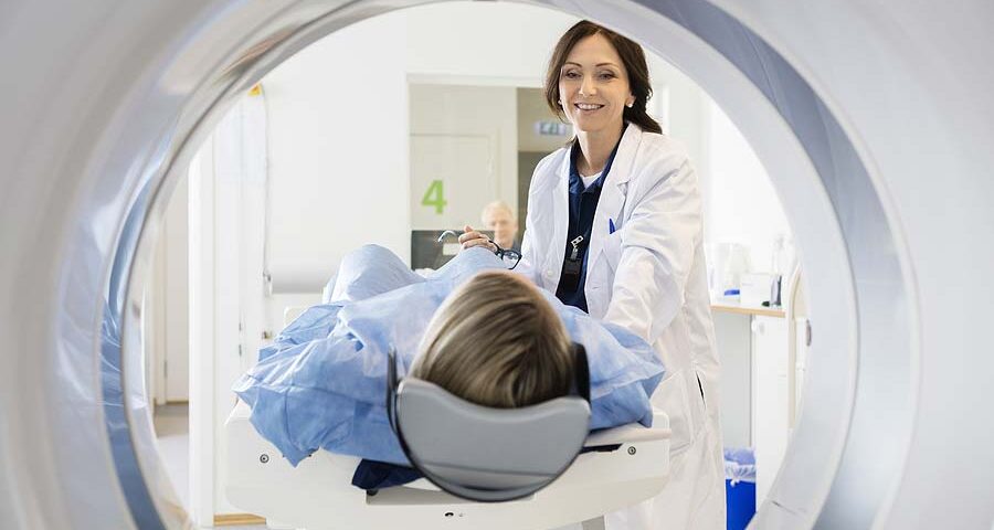 A smiling doctor positioning a patient on a CT scanner table, a procedure often compared to an MRI in terms of how long it takes.
