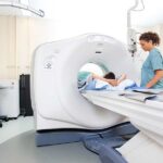 A patient lies on a CT scanner table as a healthcare professional monitors the equipment, a process similar to how long an MRI takes.
