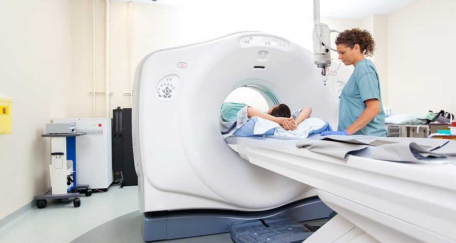 A patient lies on a CT scanner table as a healthcare professional monitors the equipment, a process similar to how long an MRI takes.